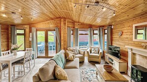 A spacious living area with a wooden ceiling, a sofa set, a dining table, and a fireplace. - Stylish two bedroom lodge, perfect for couples or families. (Cowbridge)