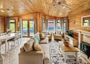 A spacious living area with a wooden ceiling, a sofa set, a dining table, and a fireplace.