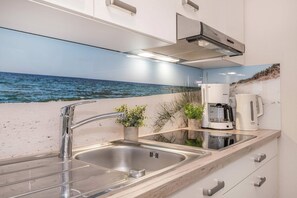 Una cocina moderna con un lavamanos de acero inoxidable, una cafetera y vistas al océano.