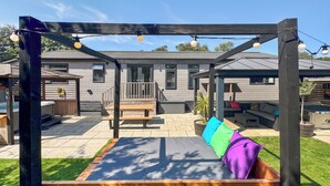 A wooden swing set with a bench, a covered seating area, and a patio with a wooden deck. - Spa Rhapsody (Sauna & Hot tub) (Raywell, Beverley)