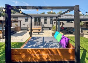 Ein hölzernes Schaukelgerüst mit einer Bank, einer überdachten Sitzgelegenheit und einer Terrasse mit Holzdeck.