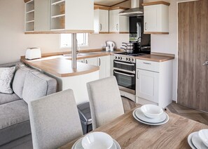 A compact kitchen with a built-in oven, a stovetop, and a sink. There is a dining table with chairs and white dishes. - 1 bedroom accommodation in Chapel St Leonards, Skegness (Chapel St Leonards, Skegness)