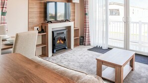 A cozy living room with a fireplace, a television, and a dining area. - 3 bedroom accommodation in Chapel St Leonards, Skegness (Chapel St Leonards, Skegness)
