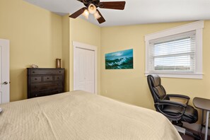 A bedroom with a bed, dresser, chair, desk, window, and a ceiling fan. - Reel Catch: Hot Tub, Close to the beach in Southern Shores! (Southern Shores)