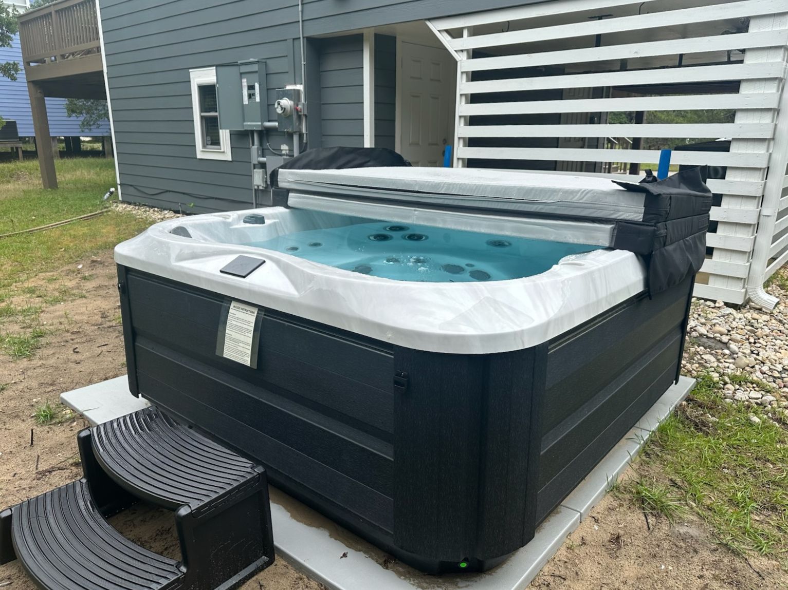A hot tub with a cover, a control panel, and a small table with chairs in front.