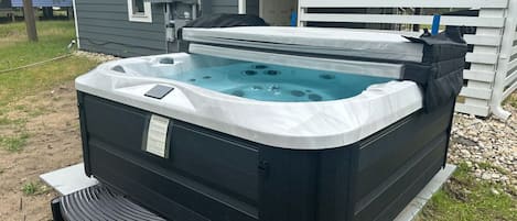 A hot tub with a cover, a control panel, and a small table with chairs in front.