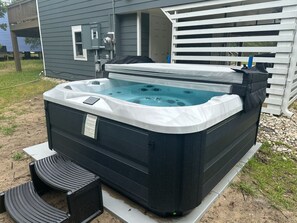 A hot tub with a cover, a control panel, and a small table with chairs in front.