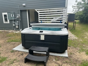 A hot tub in front of a house with a wooden deck and a small step leading up to it.
