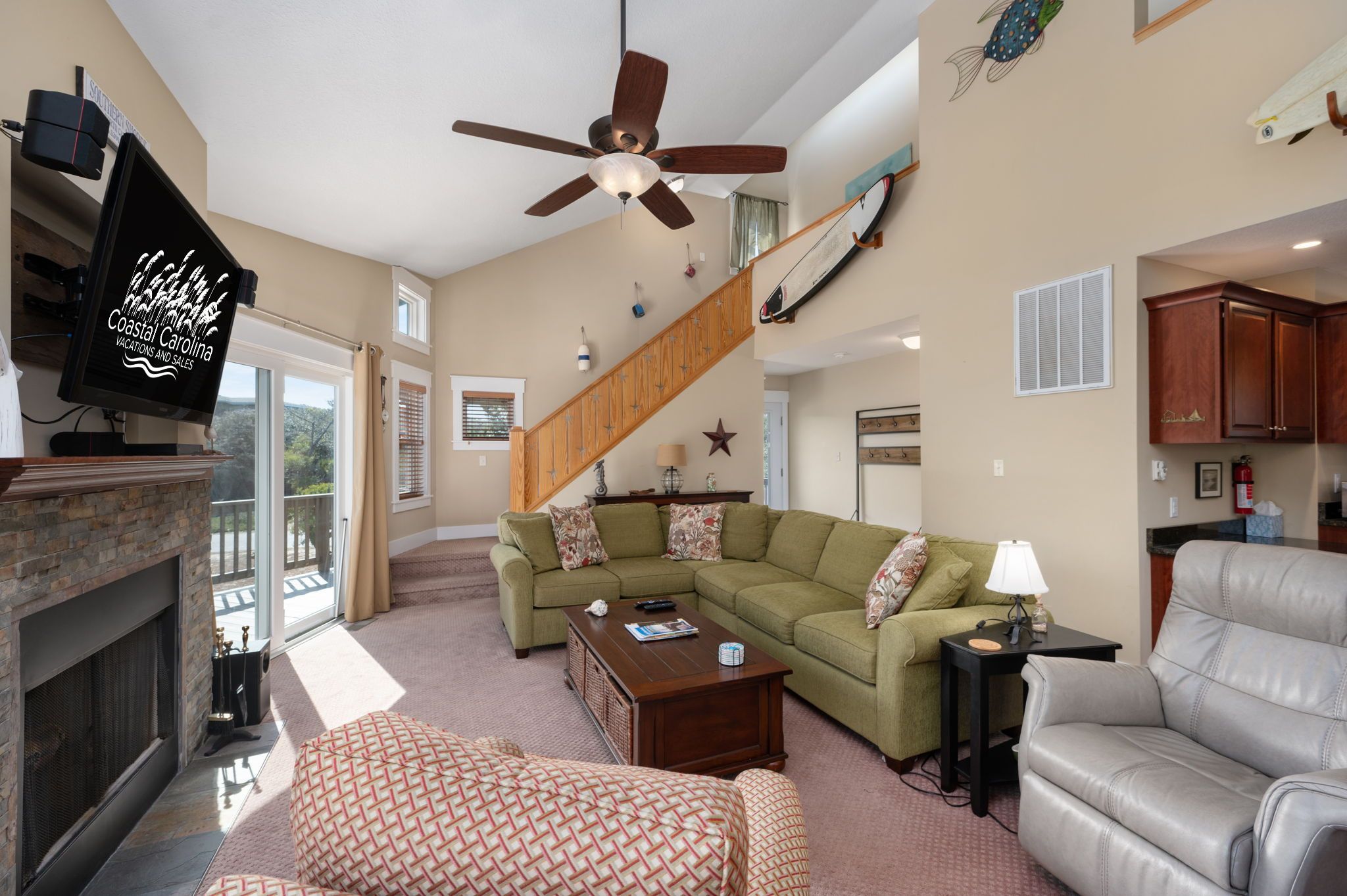 A living room with a sectional sofa, a fireplace, a ceiling fan, and a staircase.