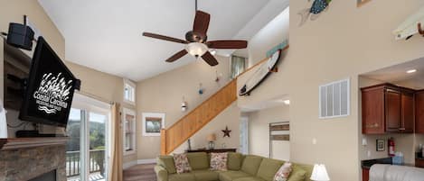 Ein Wohnzimmer mit Ecksofa, Kamin, Deckenventilator und Treppe.