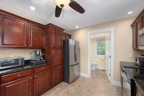 A kitchen with wooden cabinets, a stainless steel refrigerator, a built-in oven, and a ceiling fan. - Reel Catch: Hot Tub, Close to the beach in Southern Shores! (Southern Shores)