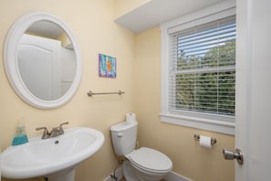 A bathroom with a round mirror, a sink, a toilet, and a window with blinds.