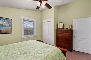 Ein Schlafzimmer mit Bett, Kommode, Tür, Fenster mit Jalousien und Deckenventilator.