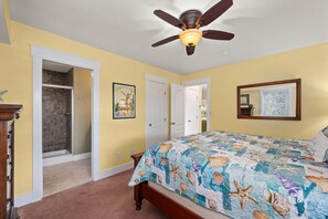 A bedroom with a bed, a ceiling fan, a door, and a wall with a framed picture.