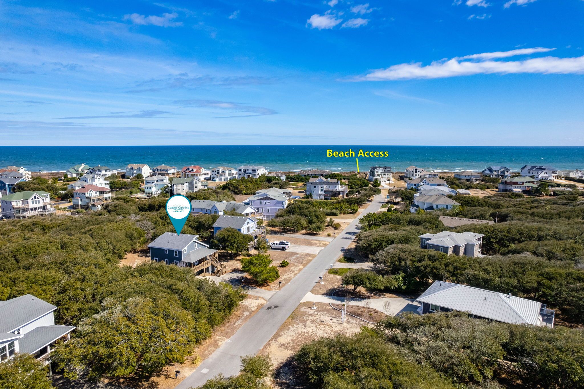 An aerial view of a coastal residential area with houses, a road, and a marked beach access point.