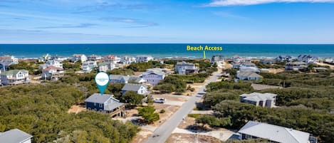An aerial view of a coastal residential area with houses, a road, and a marked beach access point.