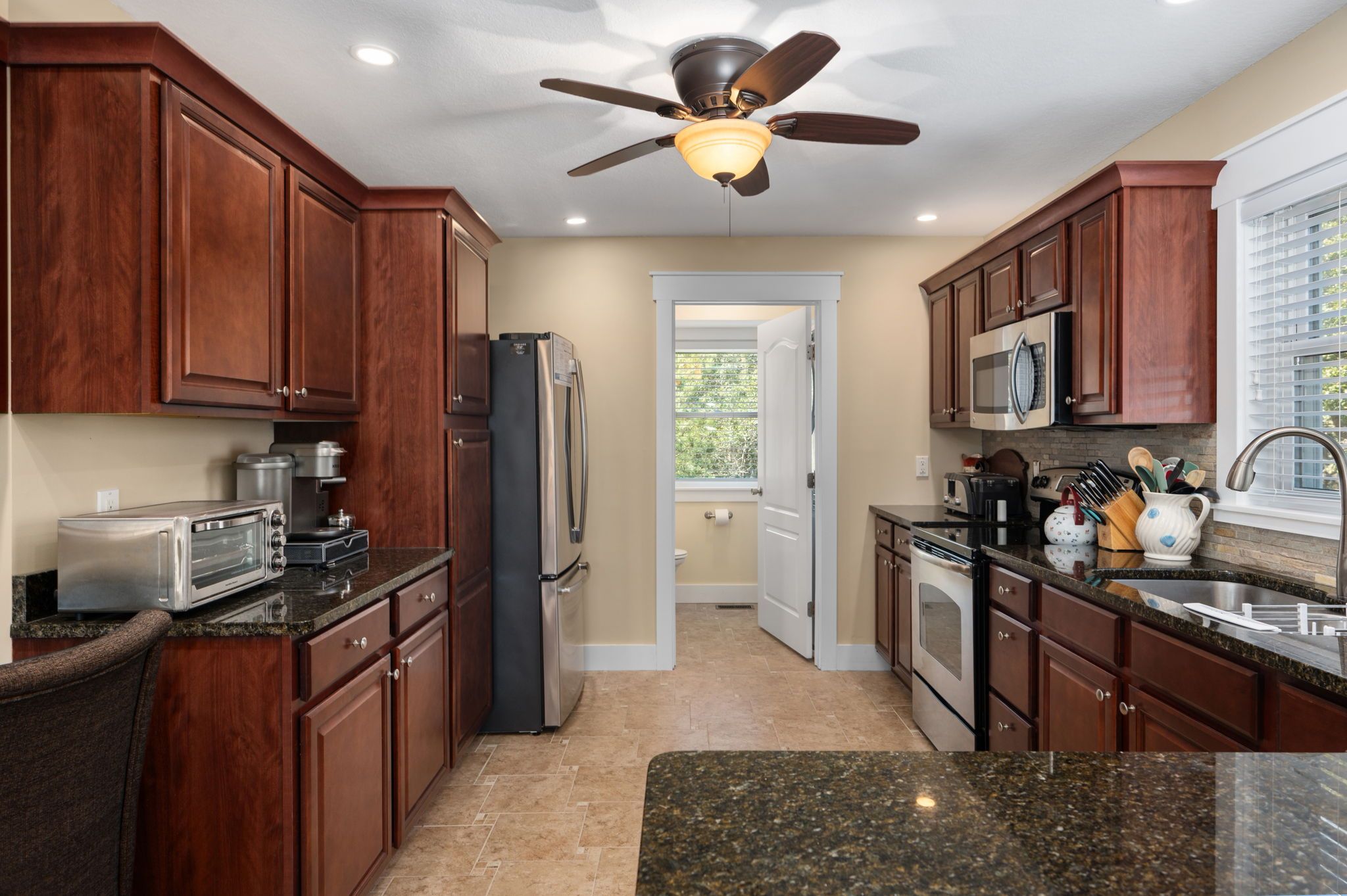 A kitchen with wooden cabinets, a refrigerator, a microwave, a stove, and a ceiling fan.