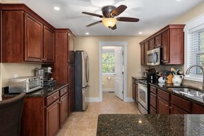 A kitchen with wooden cabinets, a refrigerator, a microwave, a stove, and a ceiling fan.