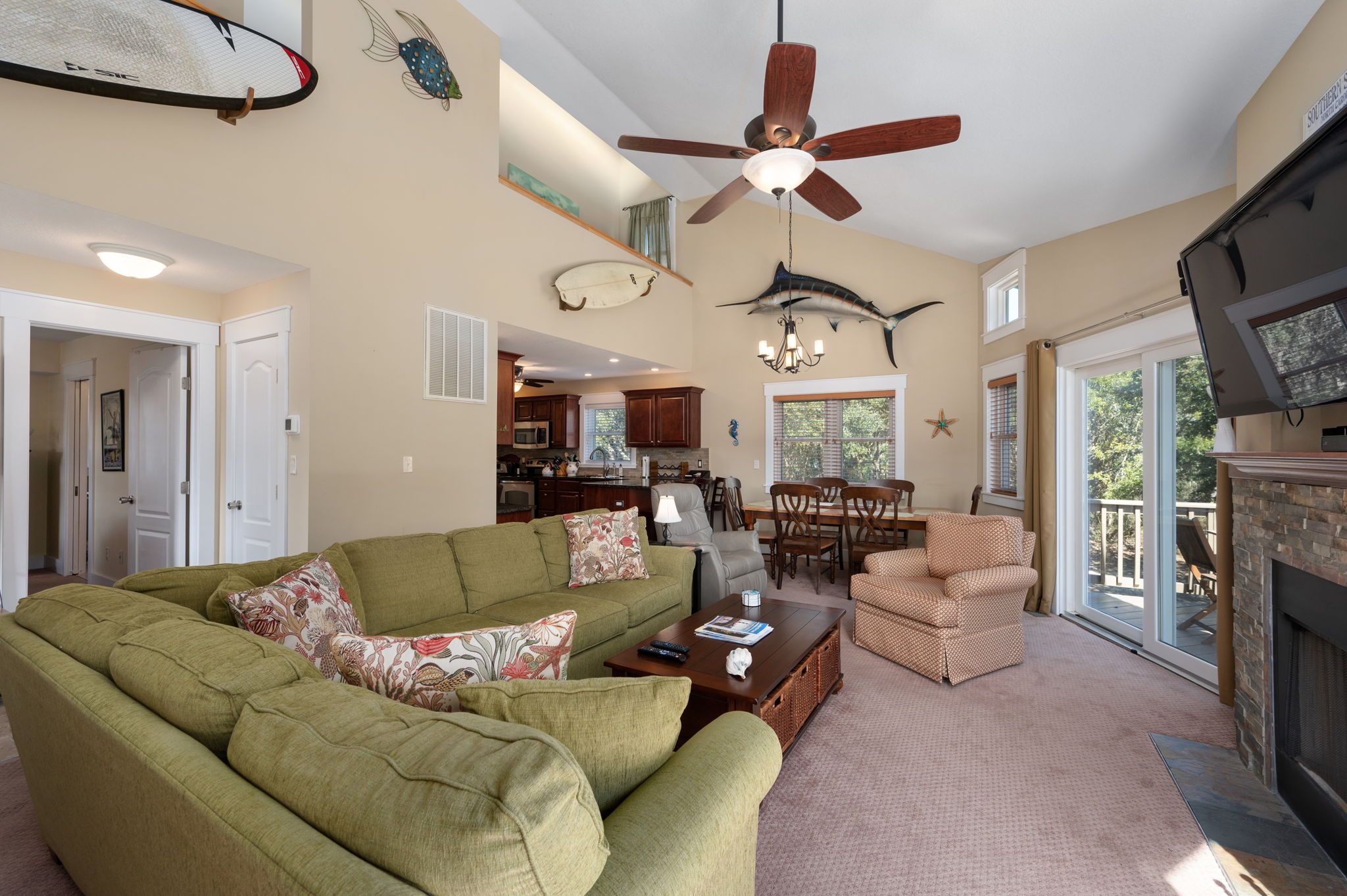 A spacious living room with a green sofa, a dining area with chairs, a ceiling fan, and a fireplace.