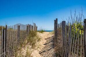 A sandy path leading to a beach, flanked by wooden fences and sparse vegetation.