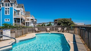 A swimming pool with a wooden deck and lounge chairs, surrounded by a wooden fence. - Sand Castle 4: Oceanfront Condo, Community Pool, Ocean Views from Deck (Kill Devil Hills)