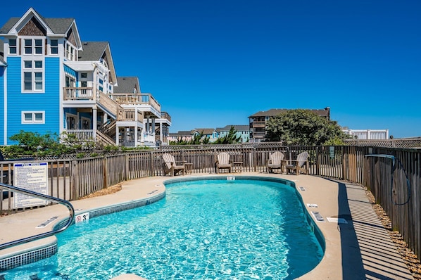 A swimming pool with a wooden deck and lounge chairs, surrounded by a wooden fence.