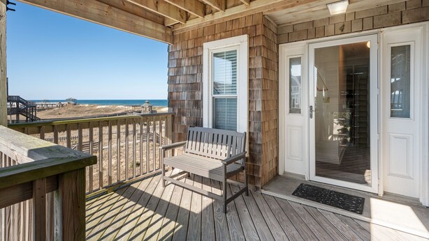 A wooden deck with a bench, a glass door, and a view of the beach. - Sand Castle 4: Oceanfront Condo, Community Pool, Ocean Views from Deck (Kill Devil Hills)