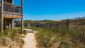 A wooden structure with a balcony, a pathway leading to a sandy beach, and a wooden fence. - Sand Castle 4: Oceanfront Condo, Community Pool, Ocean Views from Deck (Kill Devil Hills)