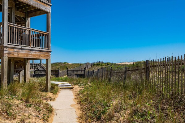 A wooden structure with a balcony, a pathway leading to a sandy beach, and a wooden fence.
