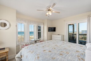 Une chambre avec un lit, un ventilateur de plafond, une télévision, une chaise, une table et une vue sur la plage.