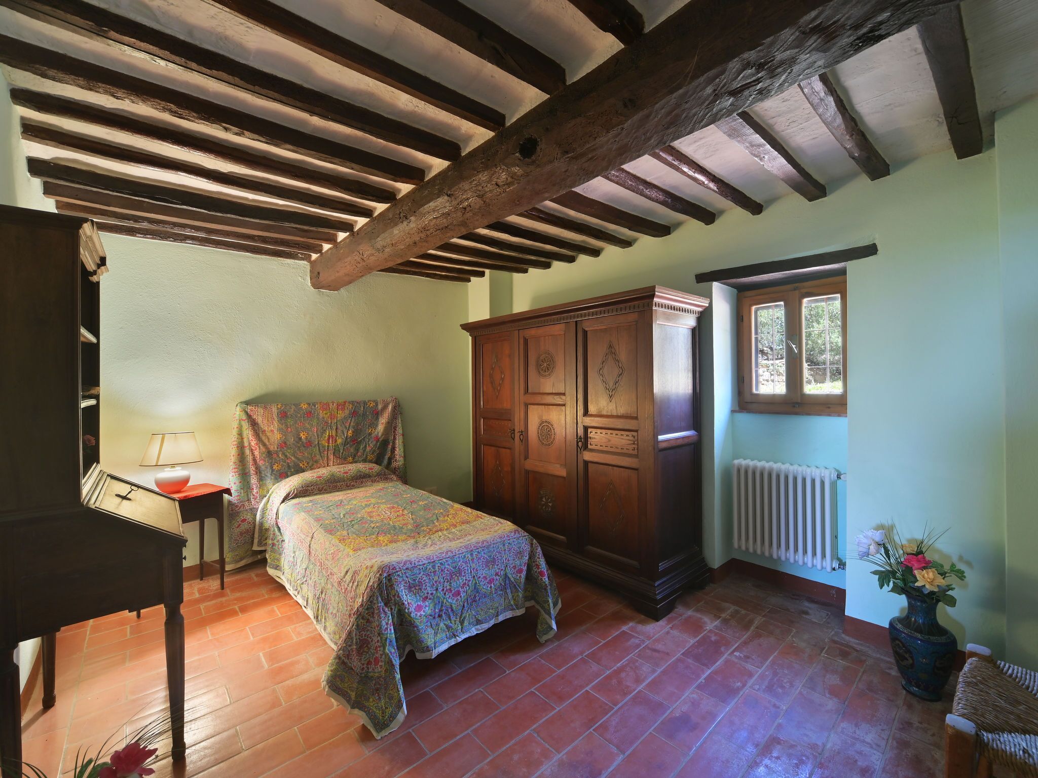 A bedroom with a wooden bed, a nightstand, a dresser, a radiator, and a window.