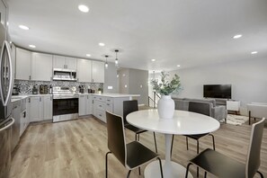 A modern kitchen with white cabinets, a built-in oven, and a microwave. There is a dining area with a round table and chairs. - Serene 4BR Getaway w/Garage, great for pets and families, hosted by DenverStays (Arvada)