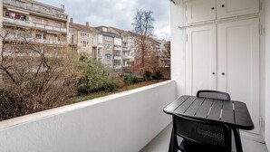 A balcony with a table and chairs, overlooking a residential area with multi-story buildings and bare trees. - Tasteful Iselin 2BR w/ Storage, steps to Central Market, by Blueground (Basel)
