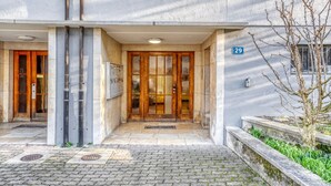 A building entrance with a wooden door, a small garden area, and a number '29' sign. - Tasteful Iselin 2BR w/ Storage, steps to Central Market, by Blueground (Basel)