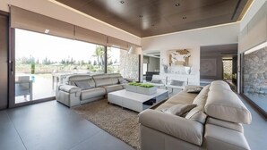 A modern living room with a sectional sofa, a coffee table, and a dining area. There is a large sliding glass door leading to an outdoor patio. - Son Rius (Muro)