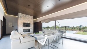 A modern living room with a stone fireplace, white sofas, a coffee table, and a view of a pool and greenery. - Son Rius (Muro)