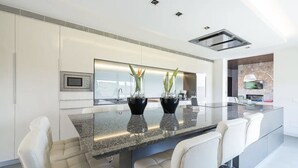 A modern kitchen with a large island, white cabinetry, and a built-in microwave. - Son Rius (Muro)