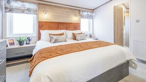 Une chambre à coucher avec une tête de lit en bois, un grand lit avec une literie blanche, une table de chevet avec une lampe et une fenêtre donnant sur un beau paysage.