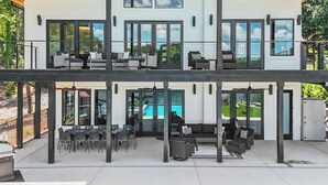 Een modern huis met twee verdiepingen, een overdekte patio, buitenmeubilair en een zwembad.