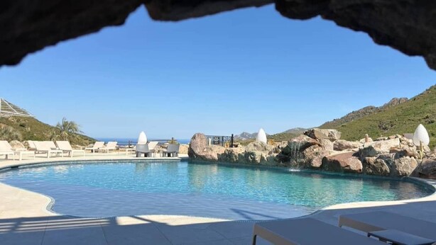 A pool with lounge chairs, a rocky landscape, and a clear sky.