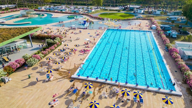A large swimming pool with multiple lanes, surrounded by sun loungers and umbrellas, with a view of a landscaped area and distant trees. - Nice apartment in villa for 4 people with A/C, WIFI, pool, TV, terrace and pets allowed (Rome)