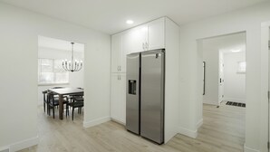 A modern kitchen with white cabinetry, a stainless steel refrigerator, and a dining area with a chandelier. - DenverStays: 5BR Stylish and Modern Home w/Garage, great for pets and families! (Arvada)