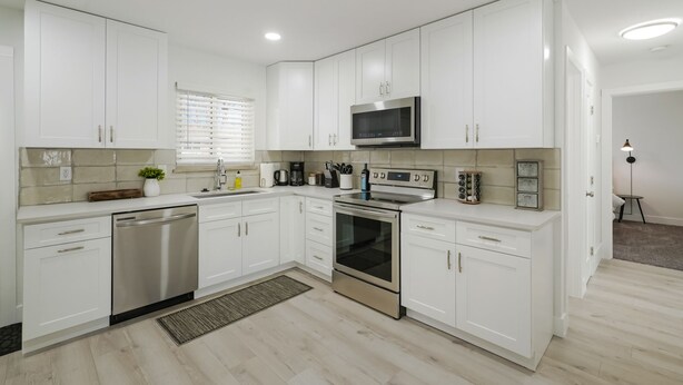 A modern kitchen with white cabinetry, stainless steel appliances, and a window with blinds. - DenverStays: 5BR Stylish and Modern Home w/Garage, great for pets and families! (Arvada)
