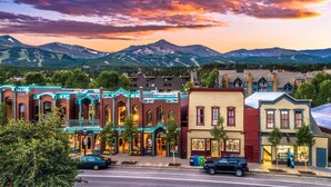 A row of buildings with a mountain backdrop, featuring a mix of architectural styles and a clear sky.