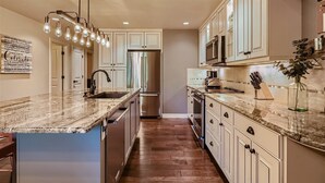 A kitchen with a marble countertop, stainless steel appliances, and a pendant light fixture.
