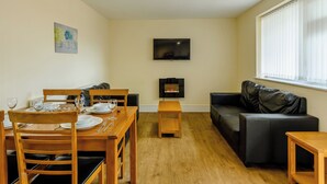 A living room with a dining area, a fireplace, a TV mounted on the wall, and a window with blinds. - Ground Floor Apartment (Pet) (Ingoldmells, Skegness)