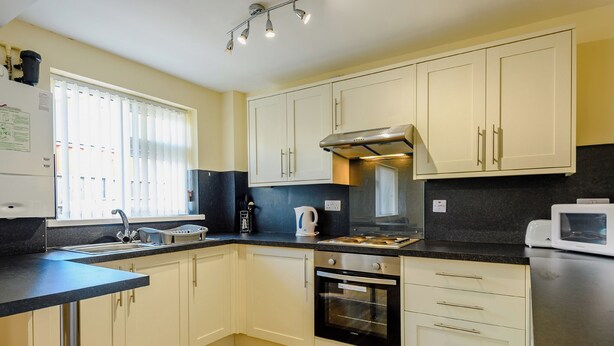 A compact kitchen with white cabinets, a black countertop, a built-in oven, and a microwave. - Ground Floor Apartment (Pet) (Ingoldmells, Skegness)