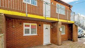 A brick building with a white door, a window with a red and yellow curtain, and a metal staircase leading to a balcony. - Ground Floor Apartment (Pet) (Ingoldmells, Skegness)