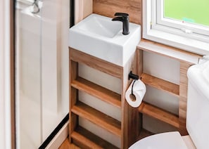 Un bagno con un lavandino bianco, mensole in legno, un water e una finestra con vista.