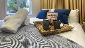 A neatly made bed with a patterned bedspread, a rolled white towel, a tray with a Nutella packet, and two black mugs. - Relax and unwind in the perfect hideout. (Snowdonia)